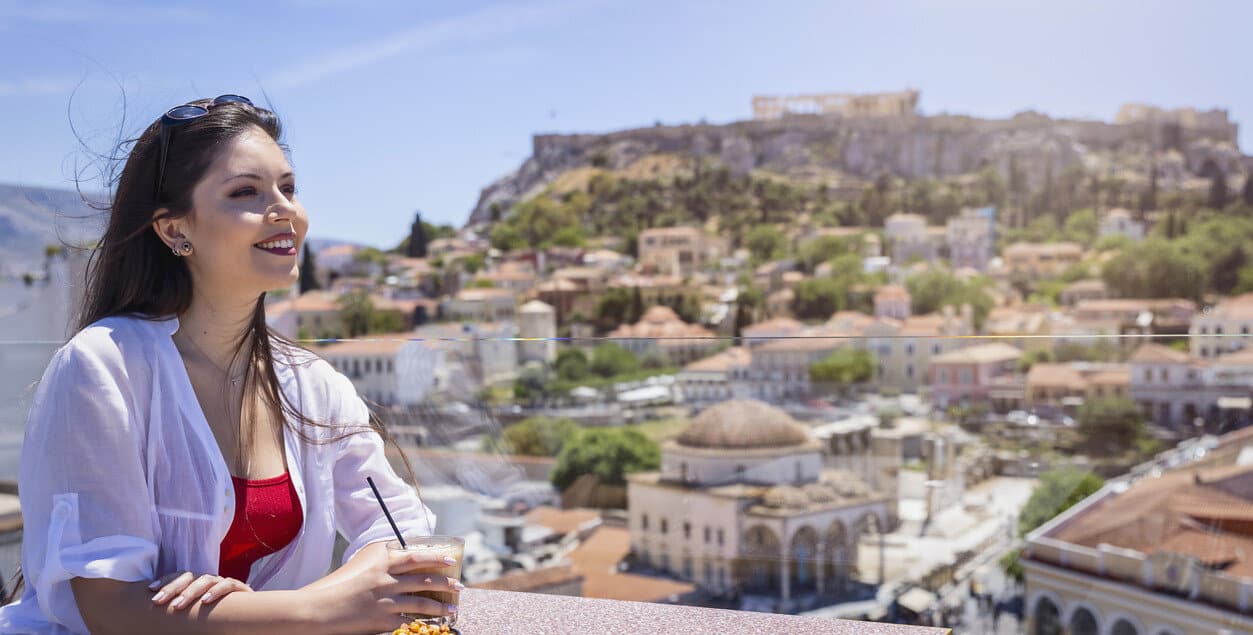 Portrait of a young, Greek woman enjoying a coffee overlooking the old town Plaka and Acropolis of Athens, Greece